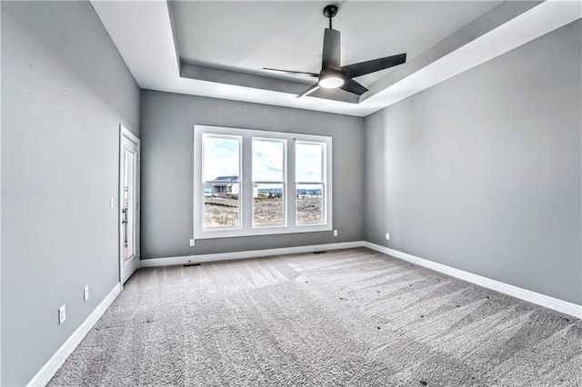 carpeted spare room with a tray ceiling and ceiling fan