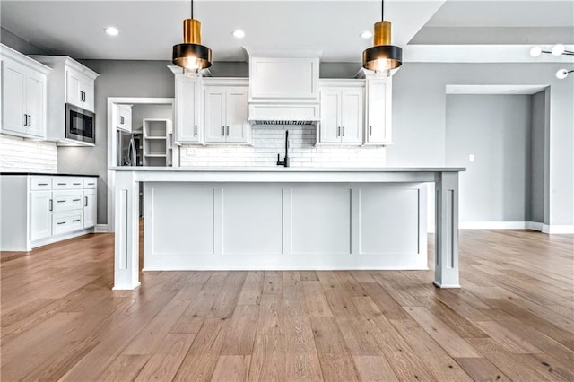 kitchen featuring white cabinets, a spacious island, built in microwave, and hanging light fixtures