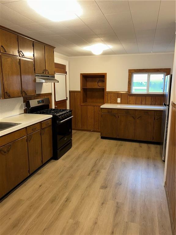 kitchen with black gas range, light wood-type flooring, stainless steel refrigerator, and wooden walls