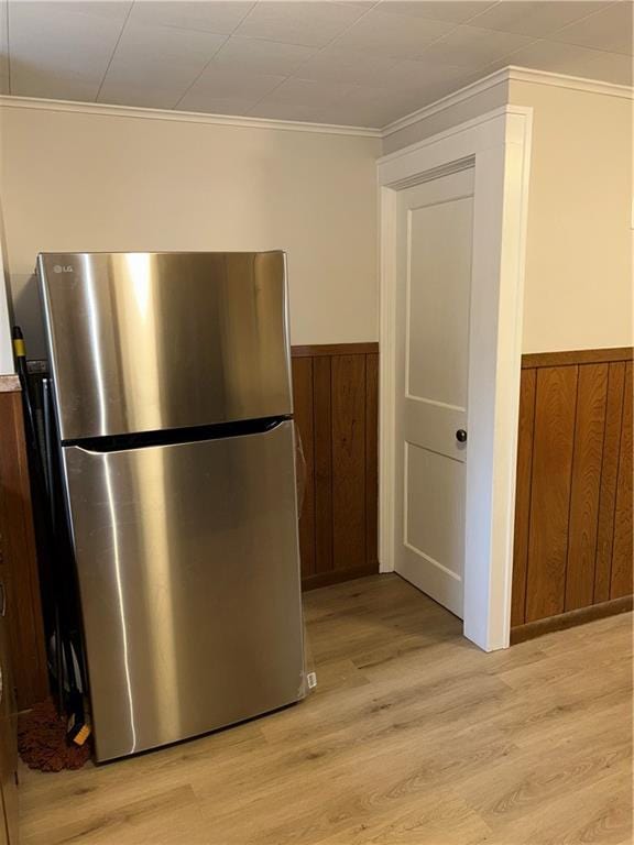 kitchen with stainless steel fridge, light wood-type flooring, ornamental molding, and wood walls