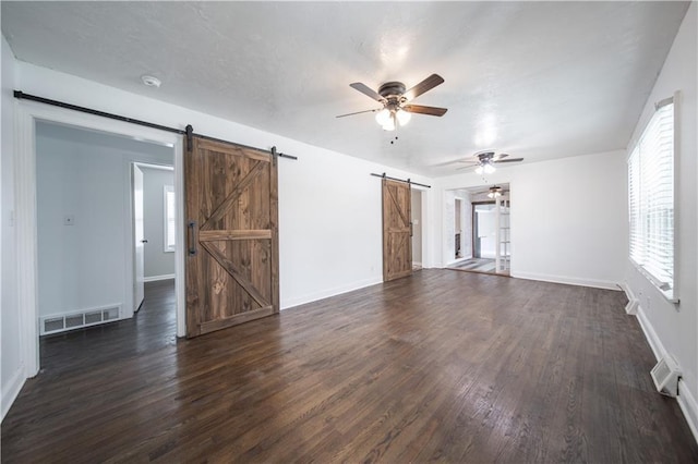 unfurnished living room with dark hardwood / wood-style floors, a barn door, and ceiling fan