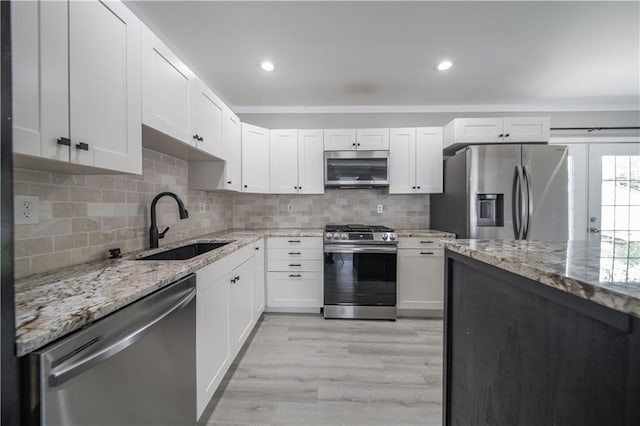 kitchen featuring light wood-type flooring, light stone counters, stainless steel appliances, sink, and white cabinetry