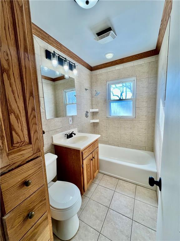 full bathroom with toilet, vanity, tile walls, tile patterned floors, and tiled shower / bath combo