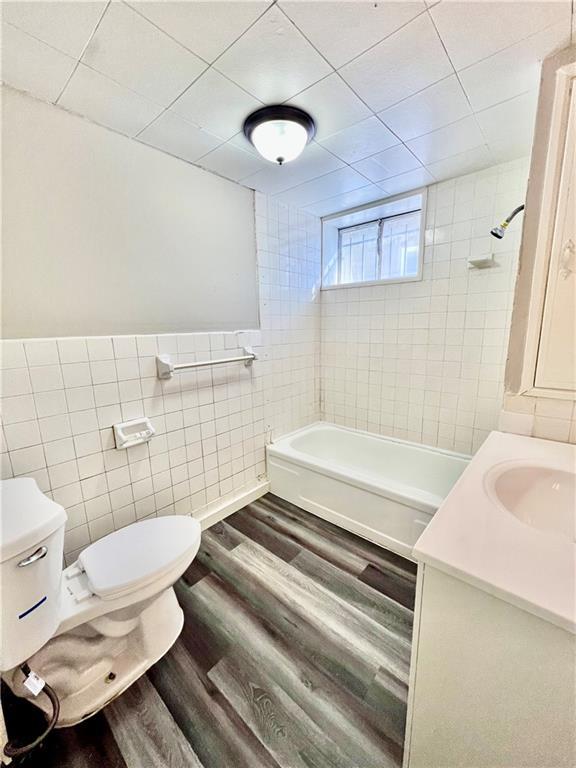 full bathroom with hardwood / wood-style floors, tiled shower / bath combo, vanity, tile walls, and toilet