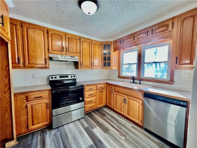 kitchen with appliances with stainless steel finishes, backsplash, light wood-type flooring, a textured ceiling, and sink