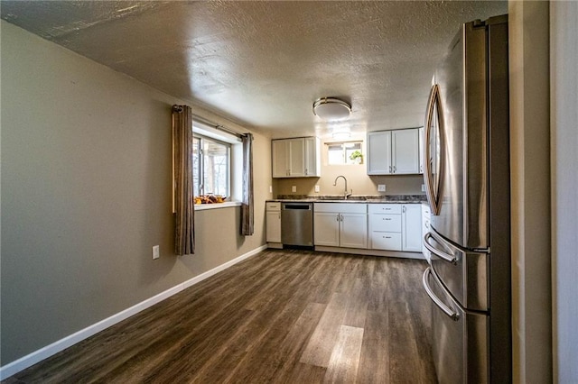 kitchen featuring appliances with stainless steel finishes, a textured ceiling, dark wood-type flooring, sink, and white cabinets