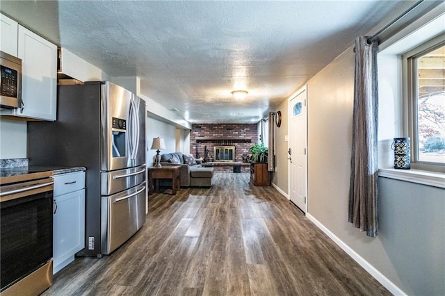 kitchen featuring a brick fireplace, a textured ceiling, white cabinetry, dark hardwood / wood-style flooring, and range