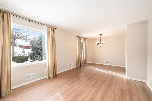 spare room featuring a healthy amount of sunlight, an inviting chandelier, and light wood-type flooring