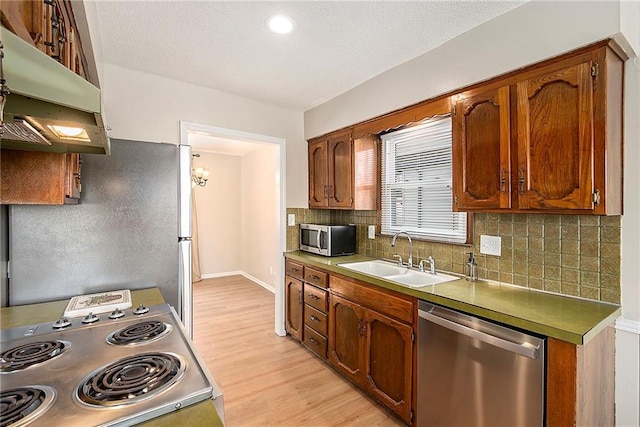 kitchen featuring appliances with stainless steel finishes, sink, backsplash, and light wood-type flooring