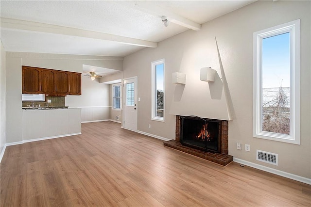 unfurnished living room featuring ceiling fan, lofted ceiling with beams, a brick fireplace, and light hardwood / wood-style flooring