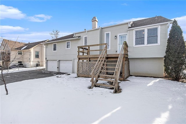 snow covered back of property featuring a wooden deck and a garage