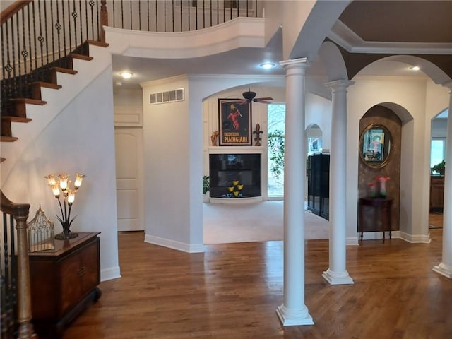 foyer entrance with decorative columns, visible vents, a ceiling fan, a glass covered fireplace, and wood finished floors