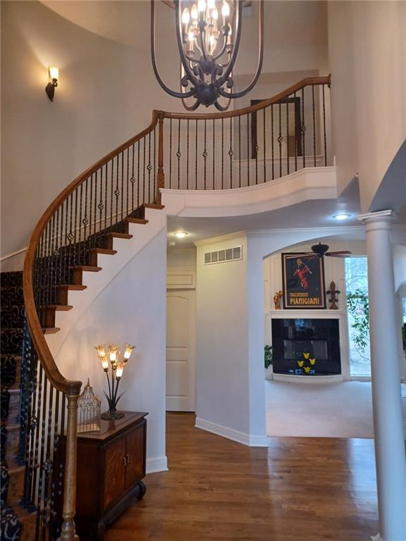 staircase with decorative columns, visible vents, a glass covered fireplace, wood finished floors, and a high ceiling