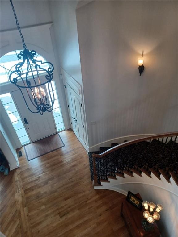 entryway with a towering ceiling, stairs, a chandelier, and wood finished floors