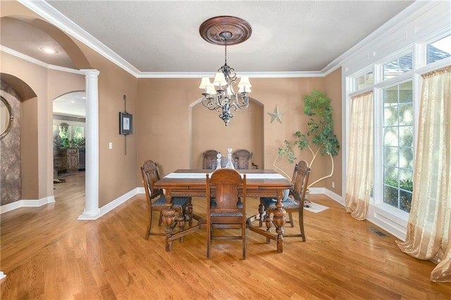 dining room featuring decorative columns, arched walkways, light wood-style flooring, ornamental molding, and a notable chandelier