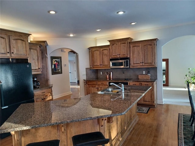 kitchen featuring a kitchen bar, arched walkways, a sink, and black appliances