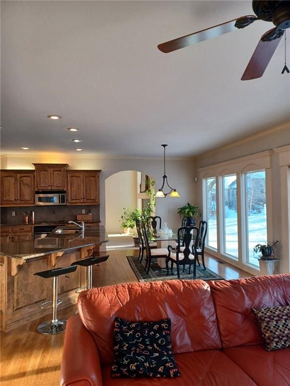 living room featuring light wood-style floors, arched walkways, a ceiling fan, and ornamental molding