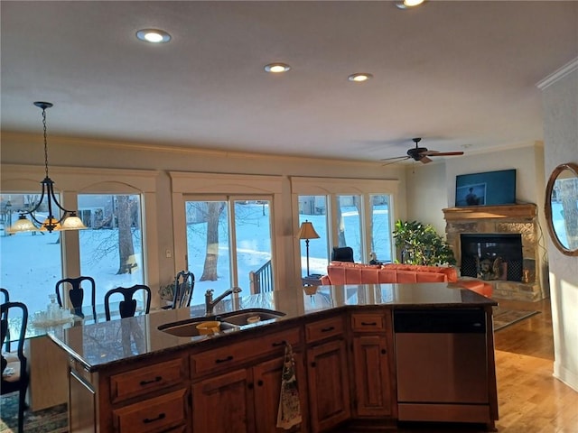 kitchen featuring light wood finished floors, a glass covered fireplace, ornamental molding, a sink, and stainless steel dishwasher