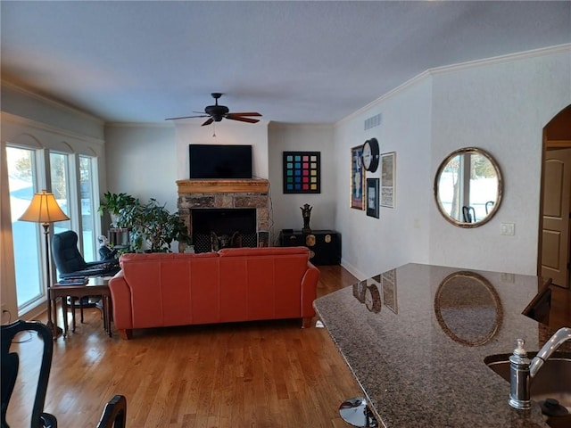 living area with crown molding, a fireplace, visible vents, ceiling fan, and wood finished floors