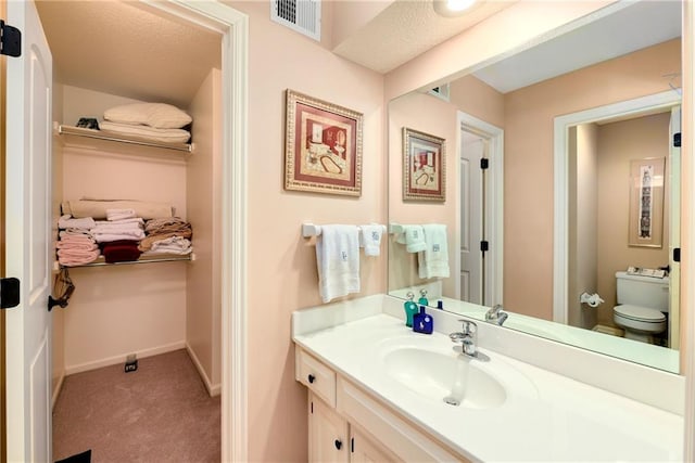 bathroom with toilet, vanity, visible vents, and baseboards