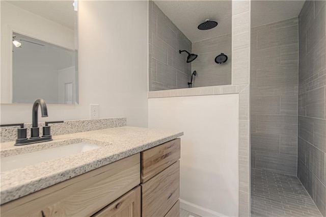 bathroom with a tile shower, vanity, and ceiling fan