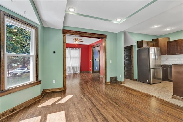 kitchen with hardwood / wood-style floors, decorative backsplash, a wealth of natural light, and stainless steel refrigerator