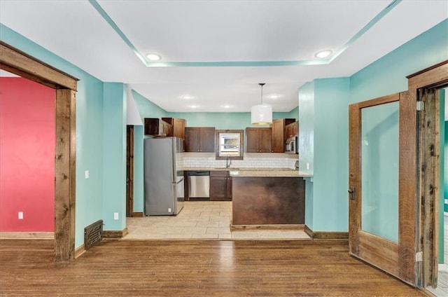 kitchen with appliances with stainless steel finishes, light wood-type flooring, tasteful backsplash, sink, and hanging light fixtures