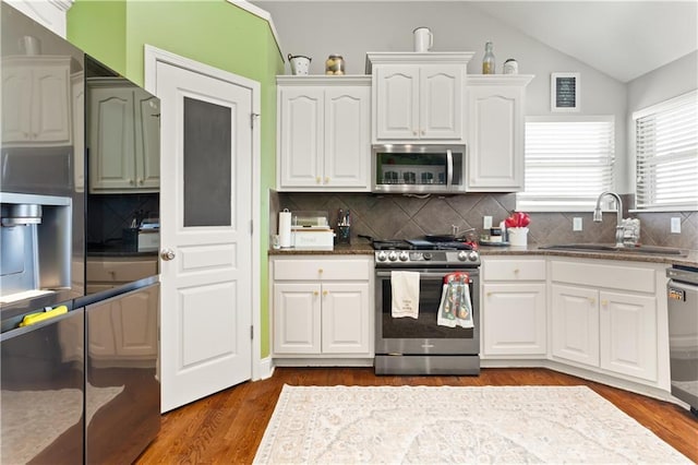 kitchen with vaulted ceiling, appliances with stainless steel finishes, white cabinetry, wood-type flooring, and sink