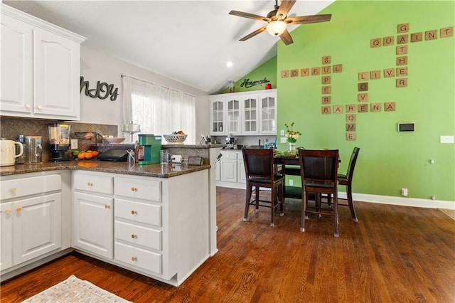 kitchen featuring dark wood-type flooring, lofted ceiling, white cabinetry, ceiling fan, and dark stone counters