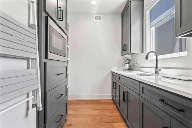 kitchen featuring gray cabinetry, sink, stainless steel microwave, and light hardwood / wood-style floors