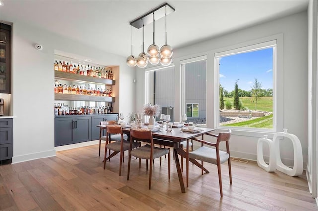 dining space featuring an inviting chandelier, indoor bar, and light hardwood / wood-style flooring