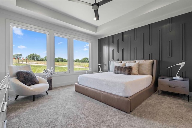 bedroom with light carpet, ceiling fan, and a tray ceiling