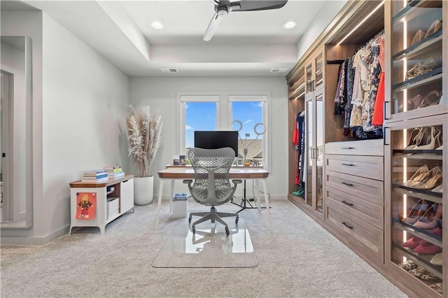 carpeted office space with a tray ceiling and ceiling fan