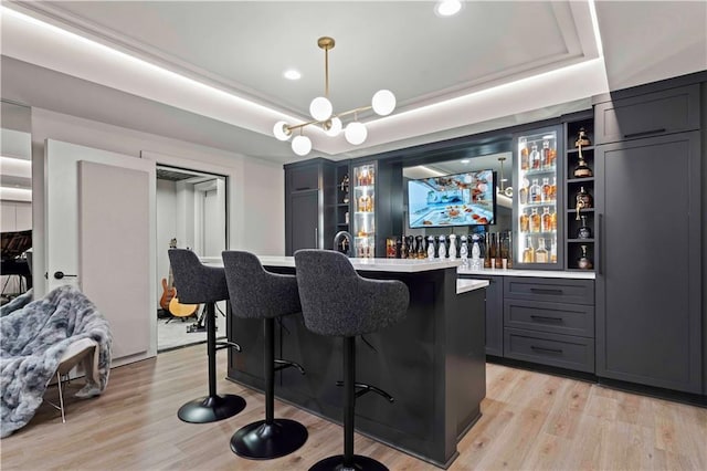 bar with pendant lighting, a tray ceiling, and light hardwood / wood-style floors