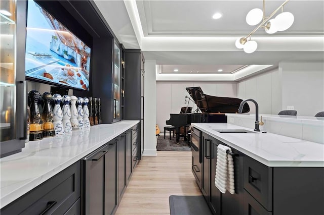 interior space with sink, hanging light fixtures, a raised ceiling, light stone countertops, and light wood-type flooring