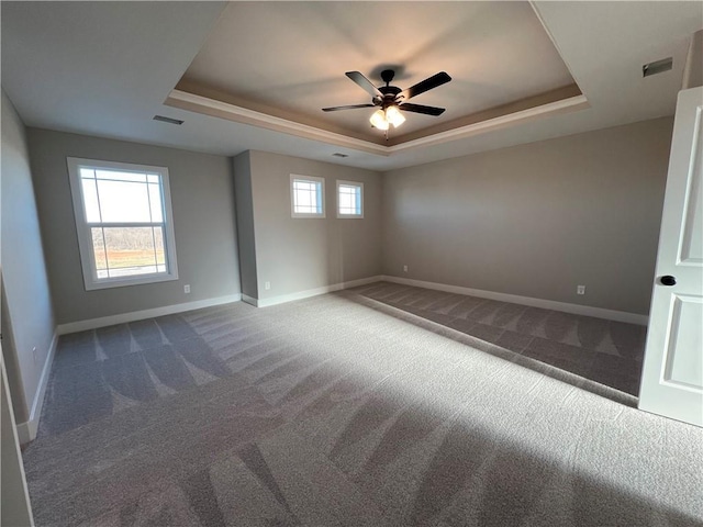 unfurnished room featuring a raised ceiling, ceiling fan, and dark carpet