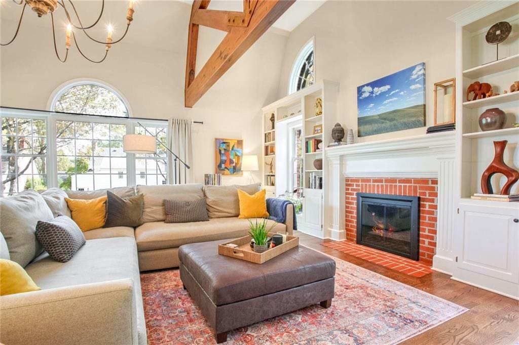 living room featuring beam ceiling, wood-type flooring, an inviting chandelier, built in features, and a fireplace