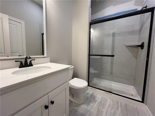 bathroom featuring a shower with door, vanity, and toilet