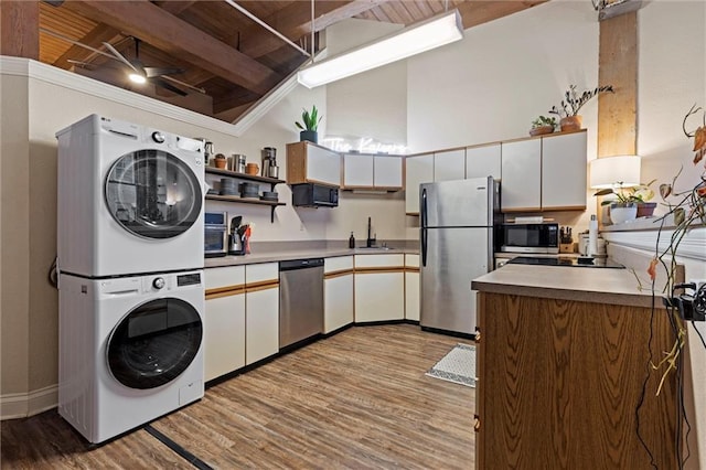 kitchen featuring ceiling fan, stacked washer and clothes dryer, wood finished floors, stainless steel appliances, and a sink