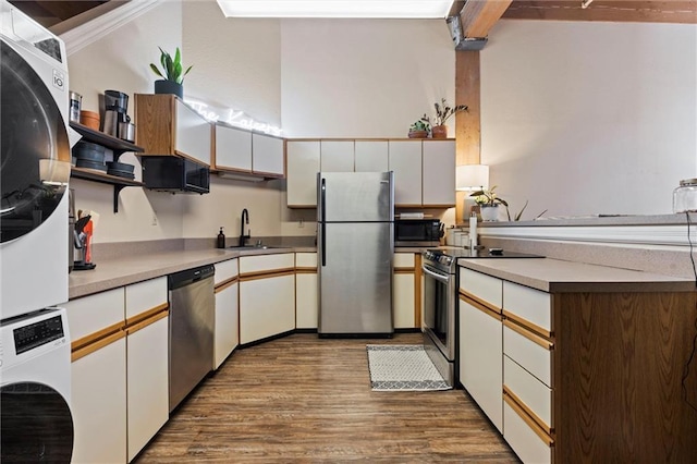 kitchen with open shelves, stacked washer and dryer, appliances with stainless steel finishes, wood finished floors, and a sink