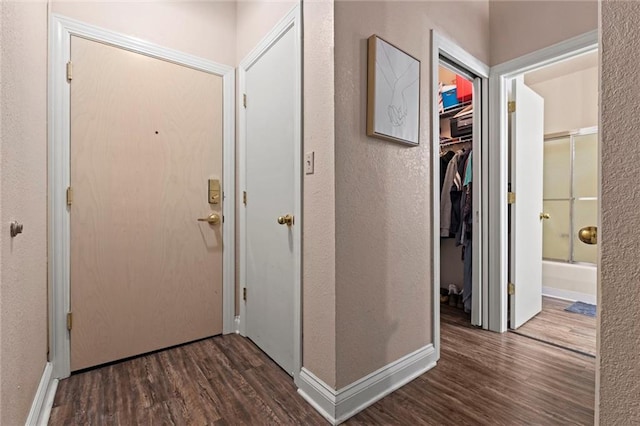 corridor with baseboards, wood finished floors, and a textured wall