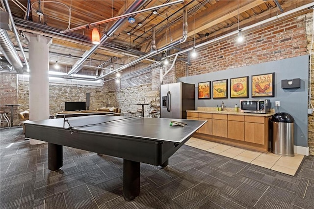 game room featuring light carpet, track lighting, a towering ceiling, and brick wall