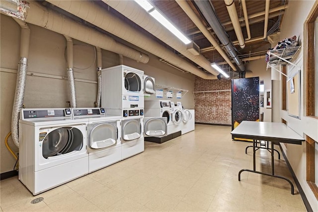 shared laundry area featuring tile patterned floors, independent washer and dryer, stacked washer and clothes dryer, and brick wall