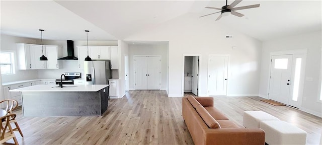 kitchen featuring pendant lighting, a kitchen island with sink, wall chimney range hood, white cabinetry, and stainless steel appliances