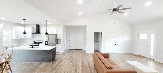 kitchen with wall chimney exhaust hood, stainless steel appliances, pendant lighting, white cabinetry, and an island with sink