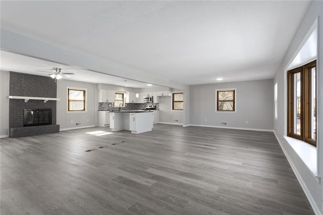 unfurnished living room with sink, dark wood-type flooring, a fireplace, and ceiling fan