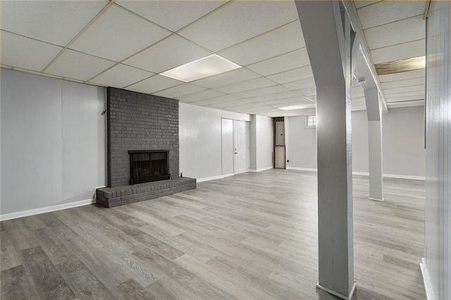 basement featuring hardwood / wood-style floors, a paneled ceiling, and a brick fireplace