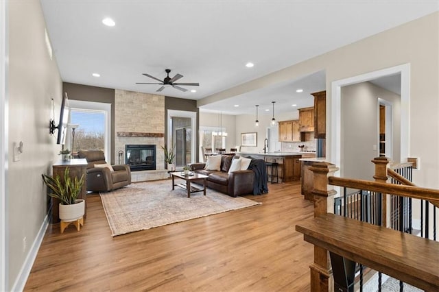 living room with plenty of natural light, ceiling fan, a stone fireplace, and light hardwood / wood-style flooring