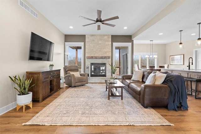 living room featuring ceiling fan with notable chandelier, light hardwood / wood-style flooring, a stone fireplace, and sink