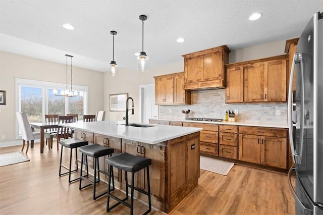 kitchen with pendant lighting, a kitchen island with sink, sink, light hardwood / wood-style floors, and stainless steel appliances